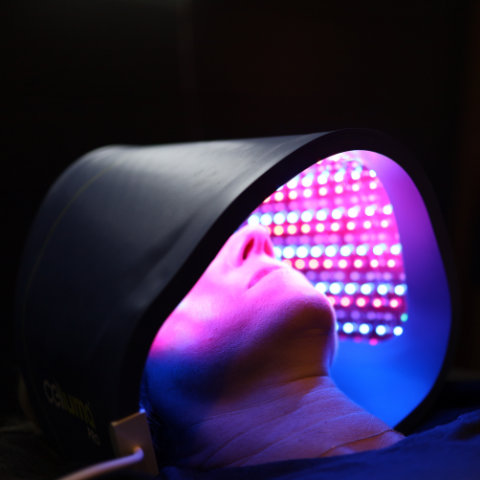 A person receiving led light therapy on their face, covered by a futuristic mask emitting multicolored lights.
