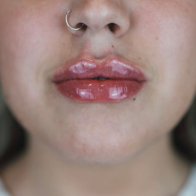 Close-up of a person's lower face showing glossy lips and a nose with a silver hoop piercing.